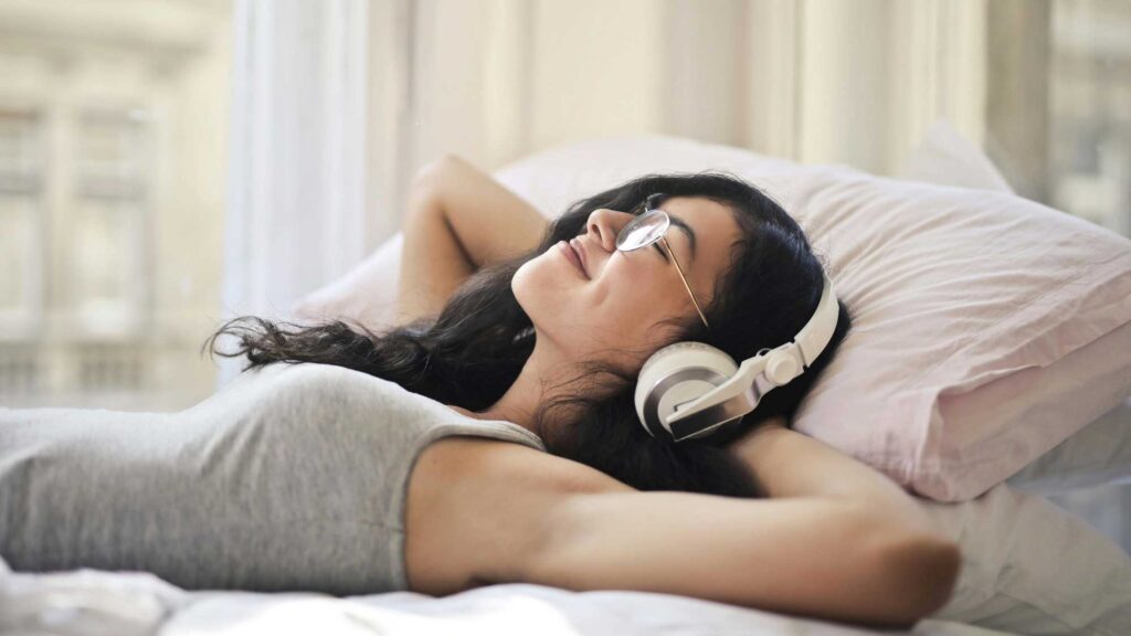 A girl laying down in bed with headphones