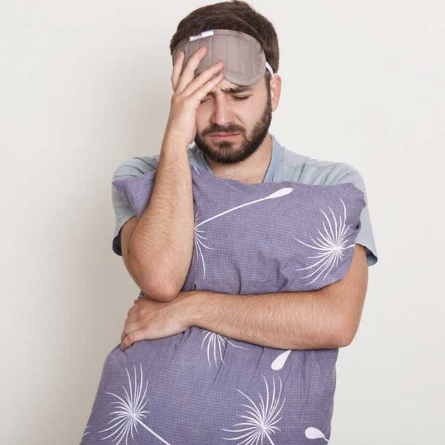 A man wearing an eye mask and holding a pillow