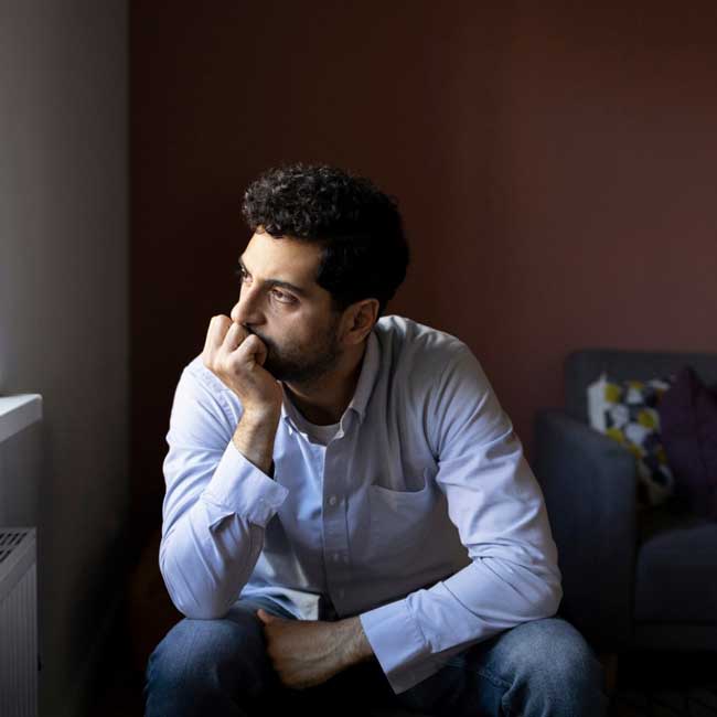 A worried man sitting on a couch looking through the window
